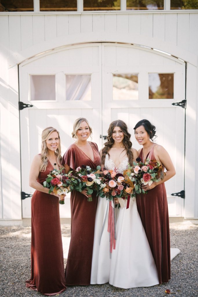 Bridesmaids dressed in rust Jenny Yoo dresses with fall floral arrangements
